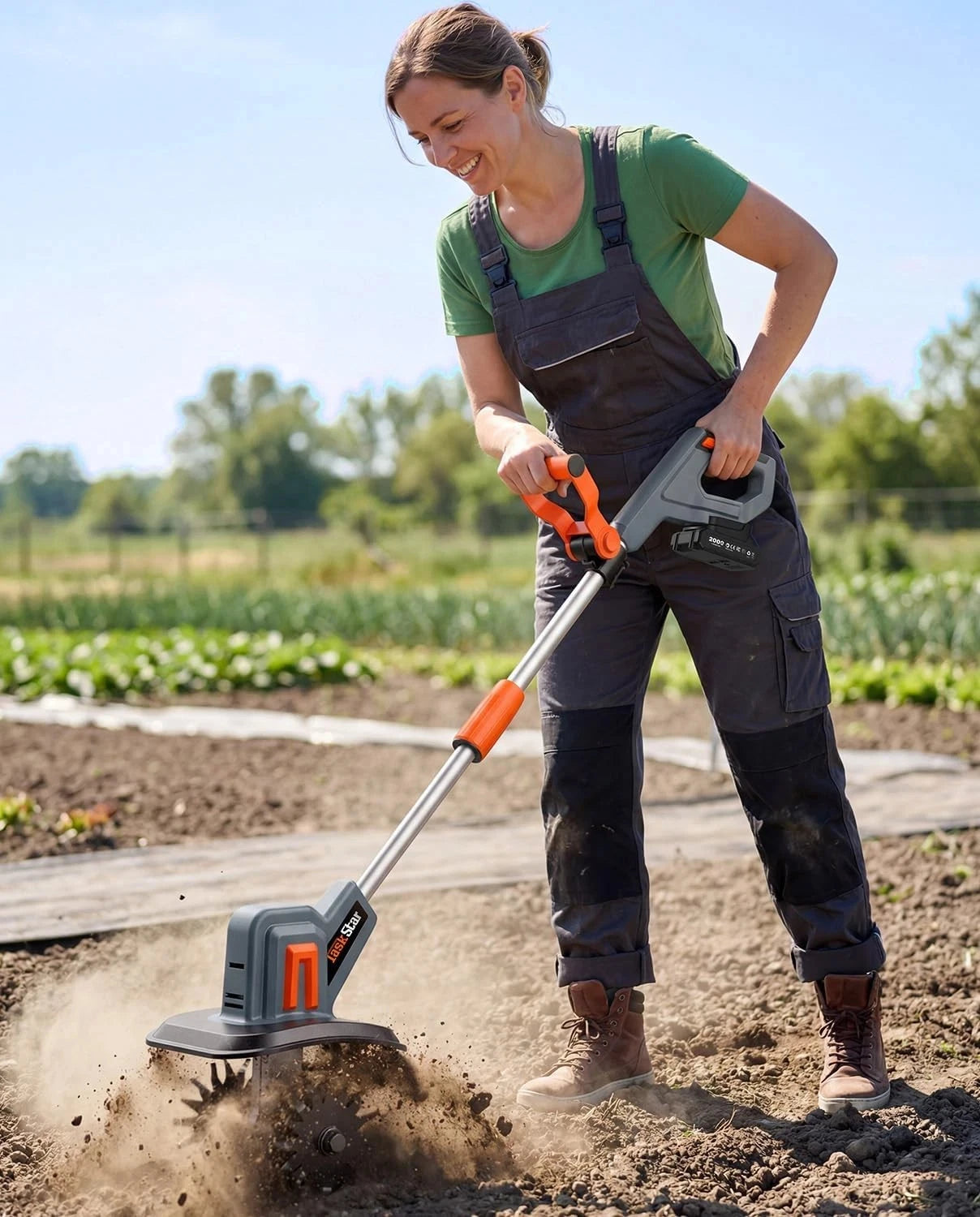 TaskStar cordless electric tiller garden cultivator with orange accents and gray body, in use outdoors.