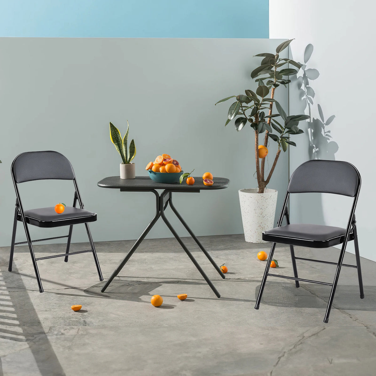 Folding chairs 4-pack with black padded seats and metal frames around a black folding table; scattered oranges indoors.