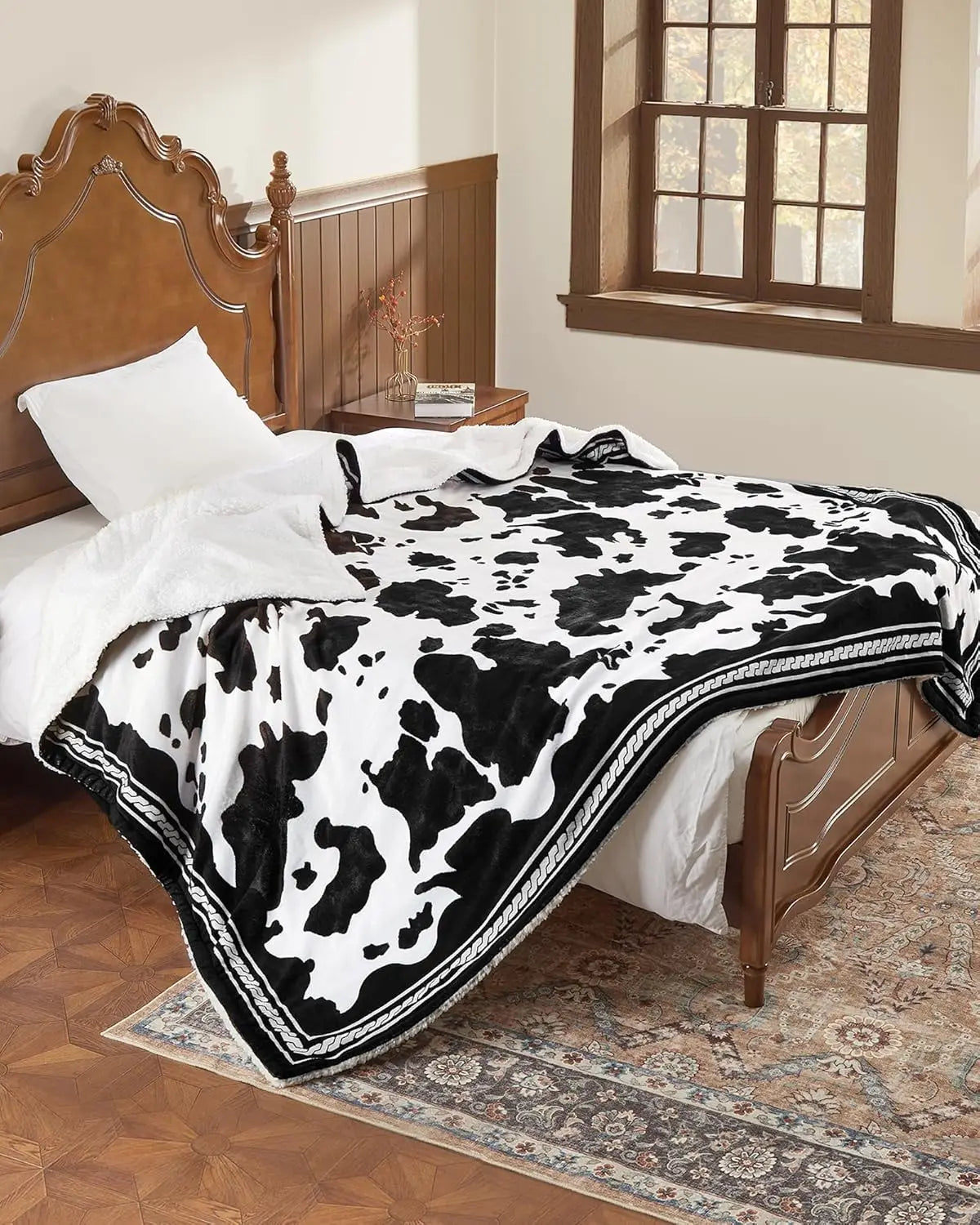 Heated electric blanket with cow-print black-and-white pattern and white plush reverse on a bed