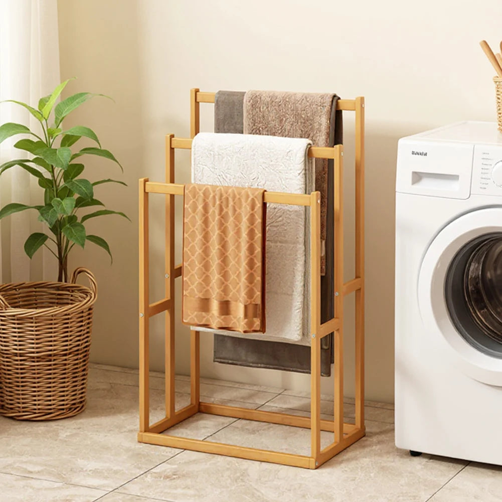 Wood vertical towel rack with 3 crossbars, light finish, towels in peach, white and brown beside a washer.