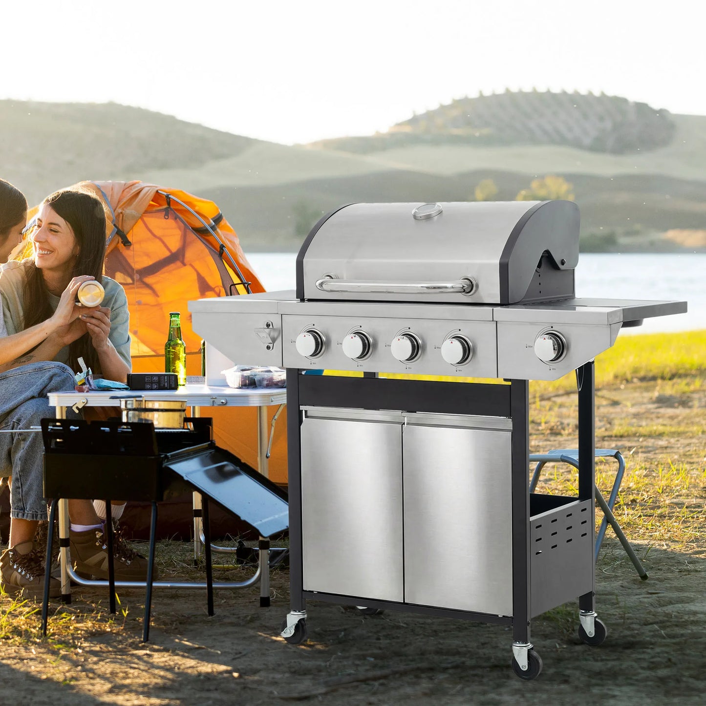 4-burner stainless steel gas grill with side burner on a freestanding cart outdoors beside a camping tent