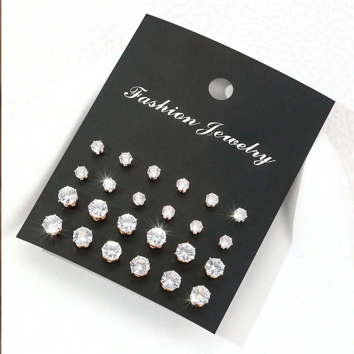 12 pairs of clear zirconia stud earrings with rose-gold settings on a black fashion jewelry display card