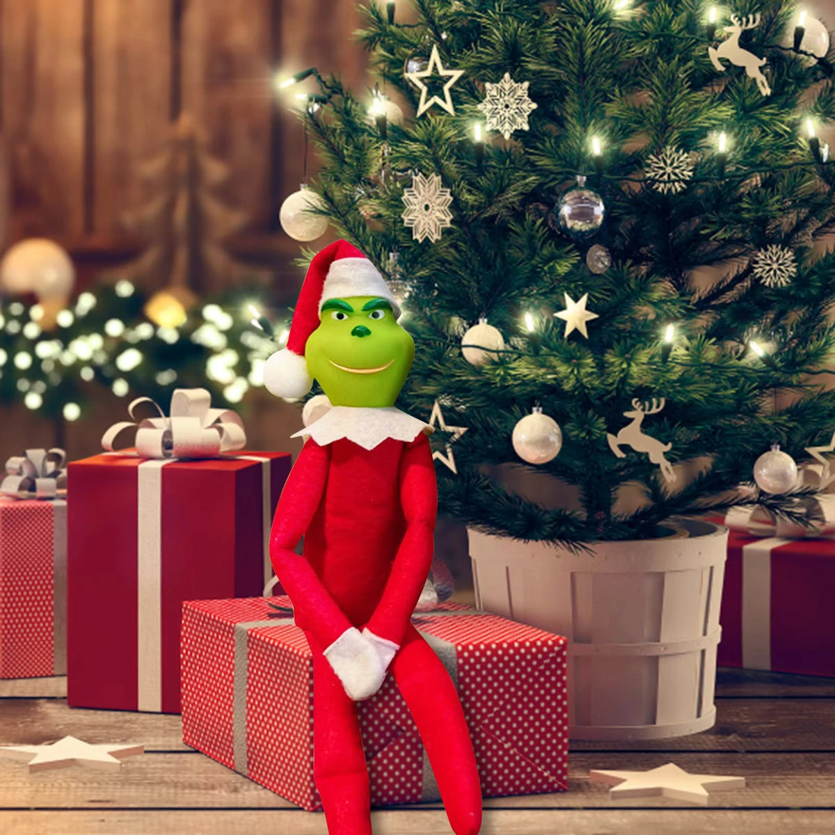 Christmas elf plush figure in red suit with Santa hat, green face, beside several gift boxes under a Christmas tree