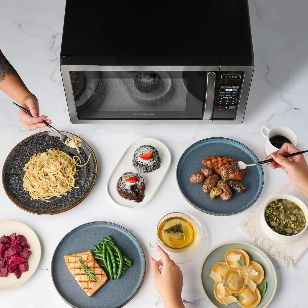 Farberware countertop microwave oven, 1.1 cu ft, 1000W, stainless steel with black top, surrounded by plated meals.