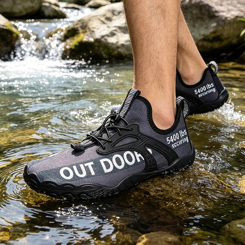 Pair of men's water shoes in black and gray, quick-dry aqua sneakers with pull tabs, shown on a rocky stream bed.