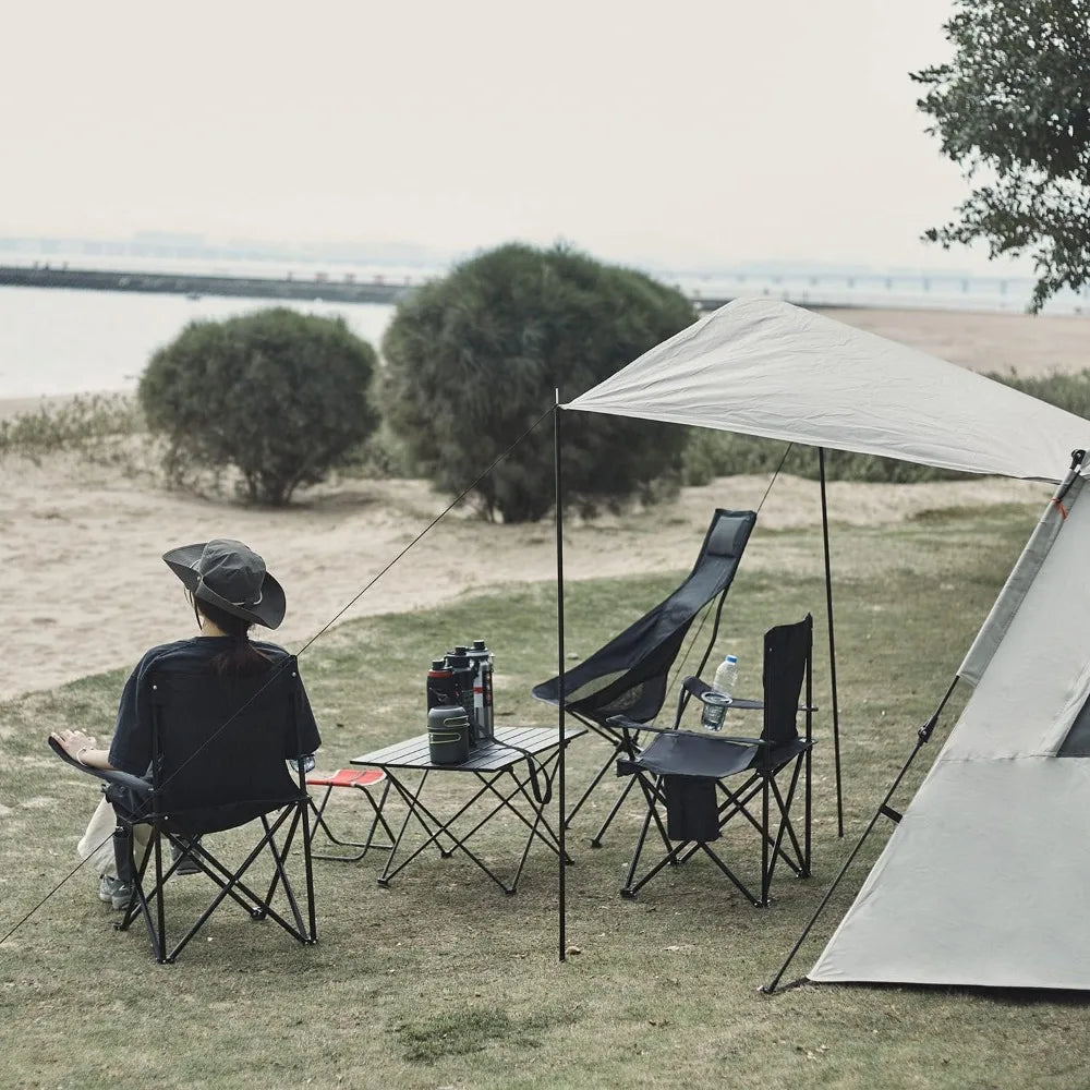 Lightweight folding camp chairs (3) in black around a small table under a canopy at the beach.