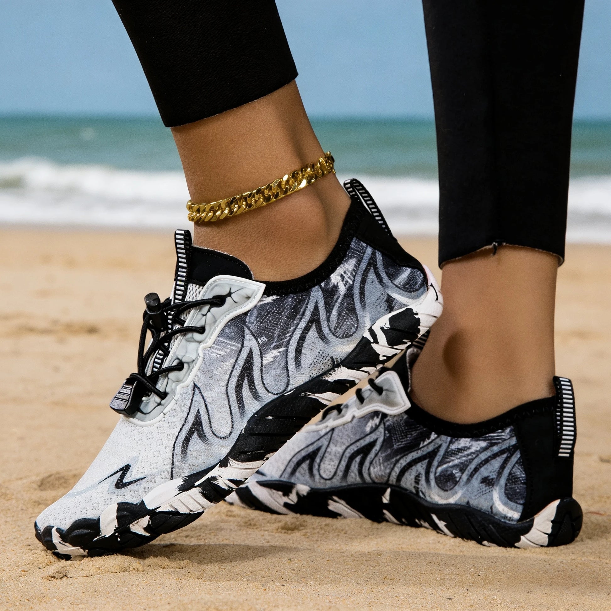 Pair of women's water shoes with gray-black zebra-print pattern on a sandy beach