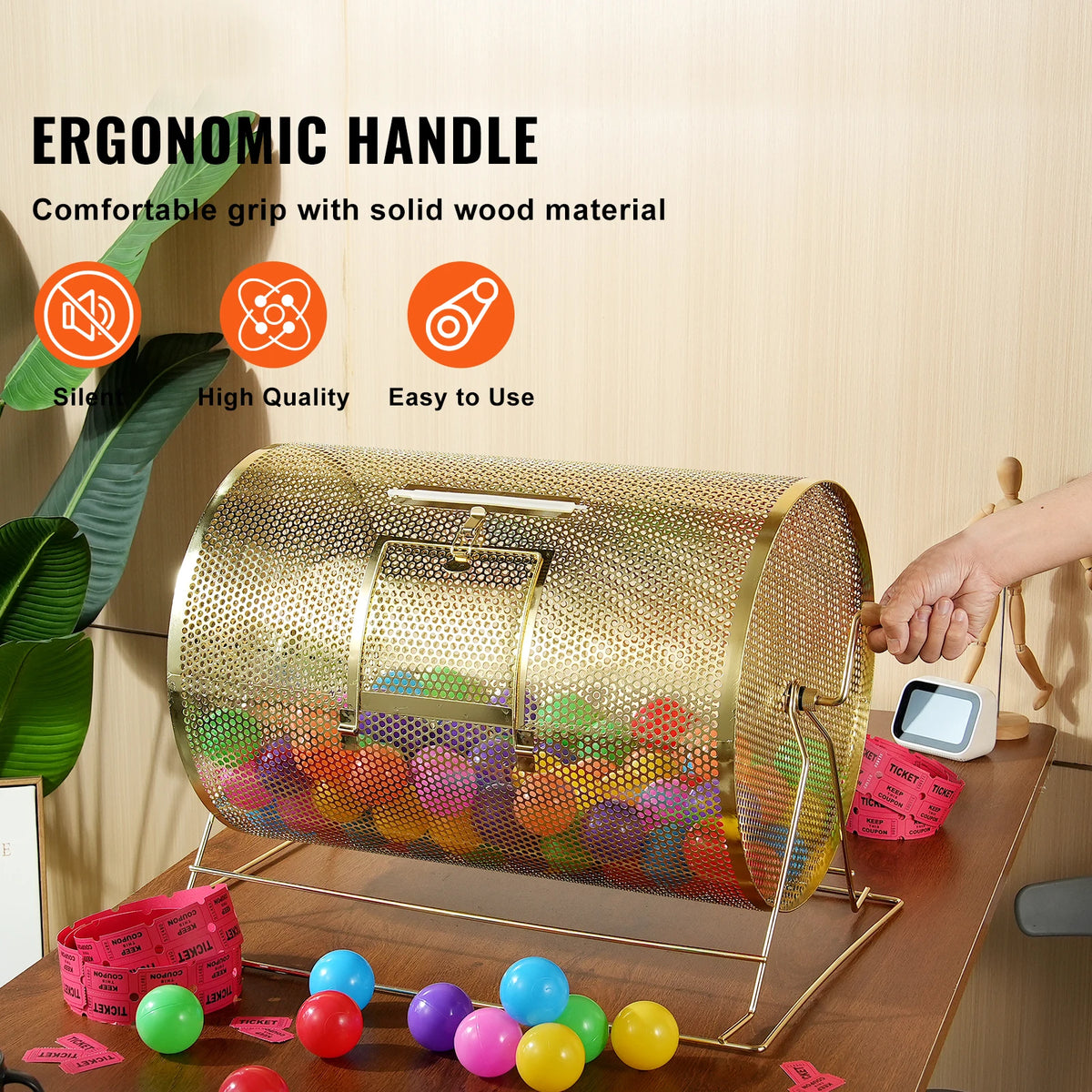 Brass-plated raffle drum with perforated spinning cage on a wooden table, filled with colorful balls and pink tickets.