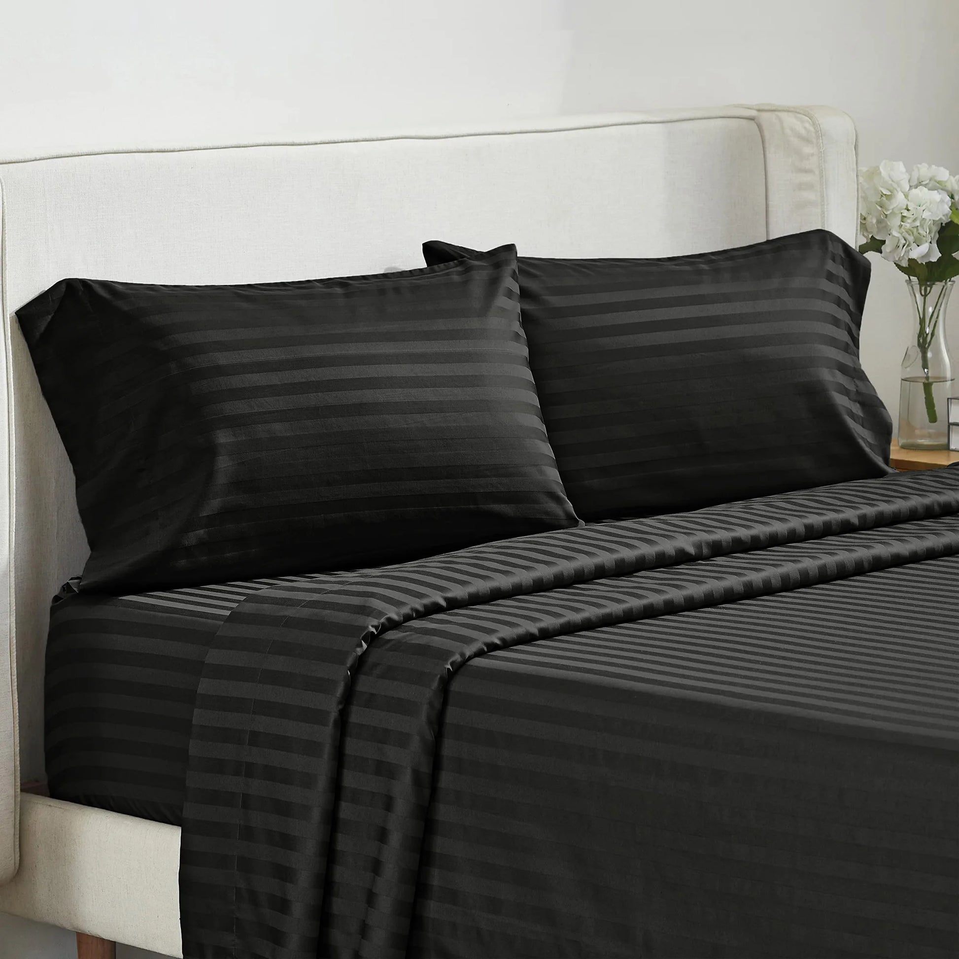 Battilo 4-piece bed sheet set with striped black-gray pillowcases on a bed with a beige upholstered headboard