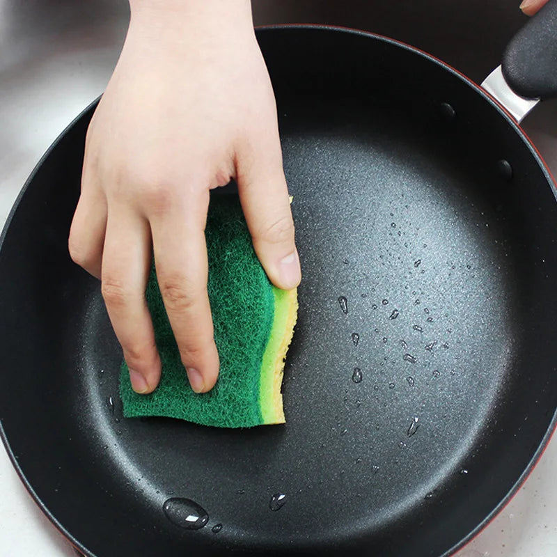 Multi-layer kitchen sponge scrub in green and yellow used to clean a nonstick frying pan
