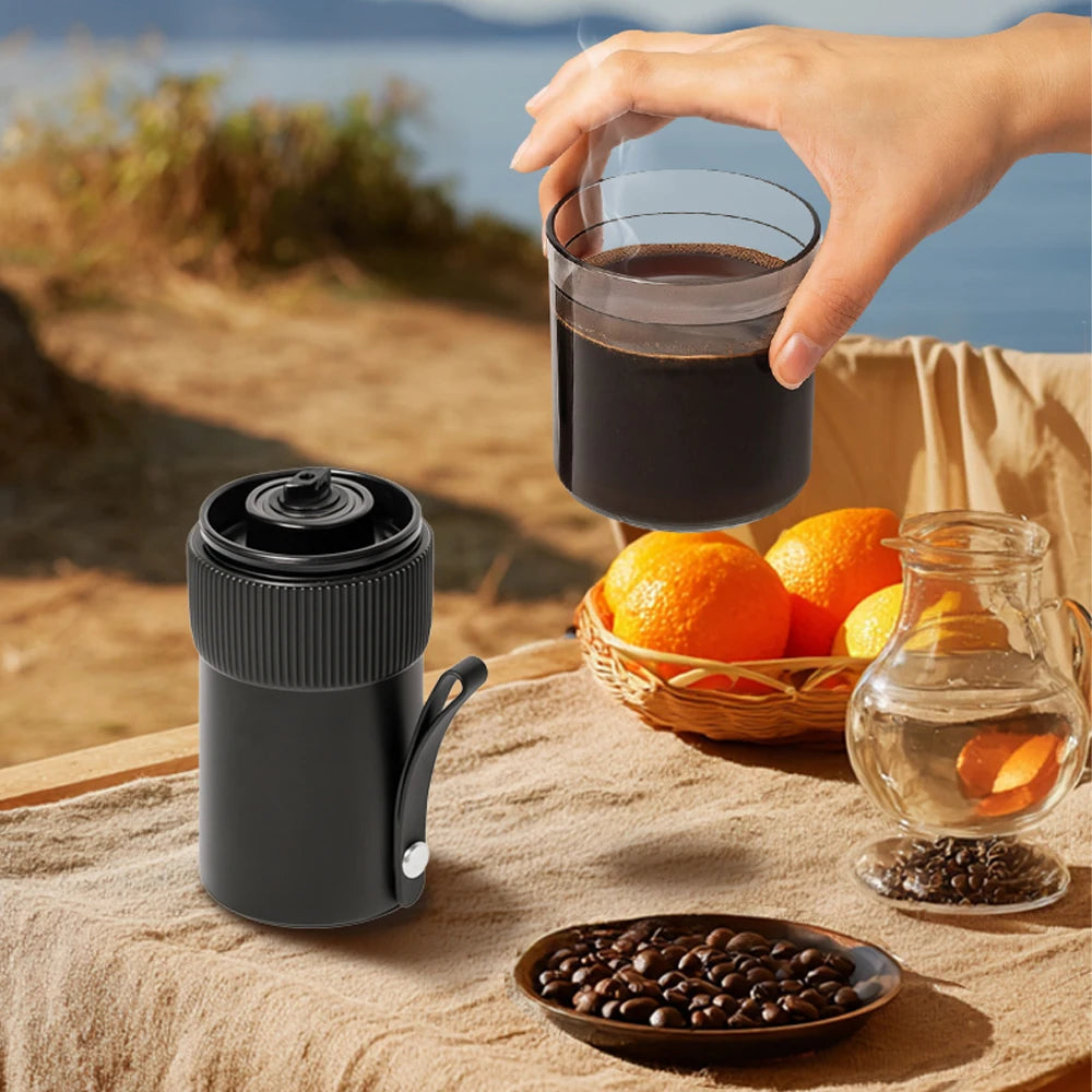 Portable electric coffee grinder, black and compact, with a cup of coffee and coffee beans nearby.