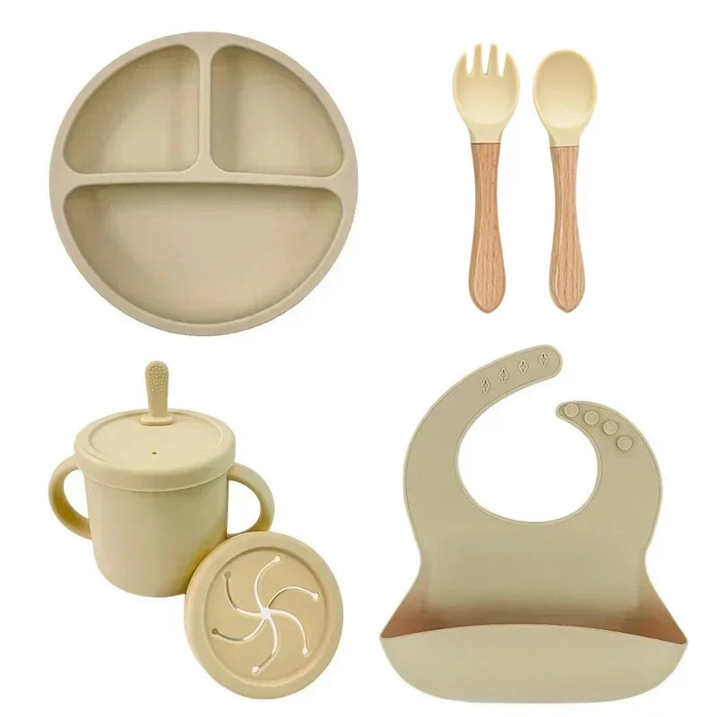 Beige silicone baby feeding set with 1 divided suction plate, sippy cup, wooden-handle spoon and fork, silicone bib.