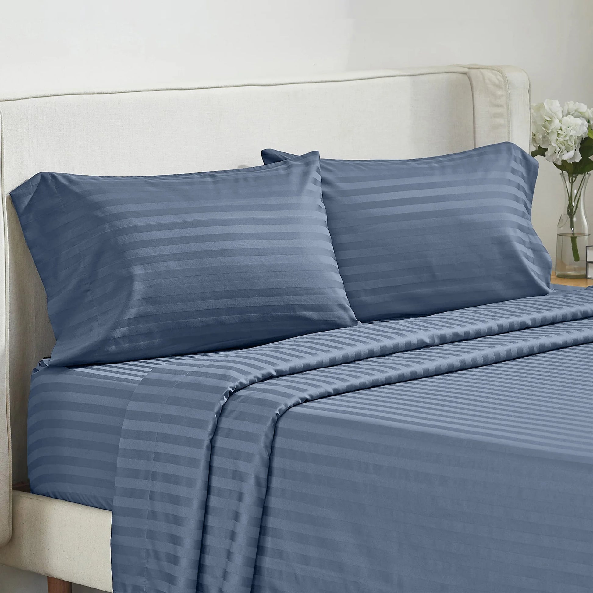 Bed sheet set blue striped with pillowcases, 4-piece, on a light upholstered bed