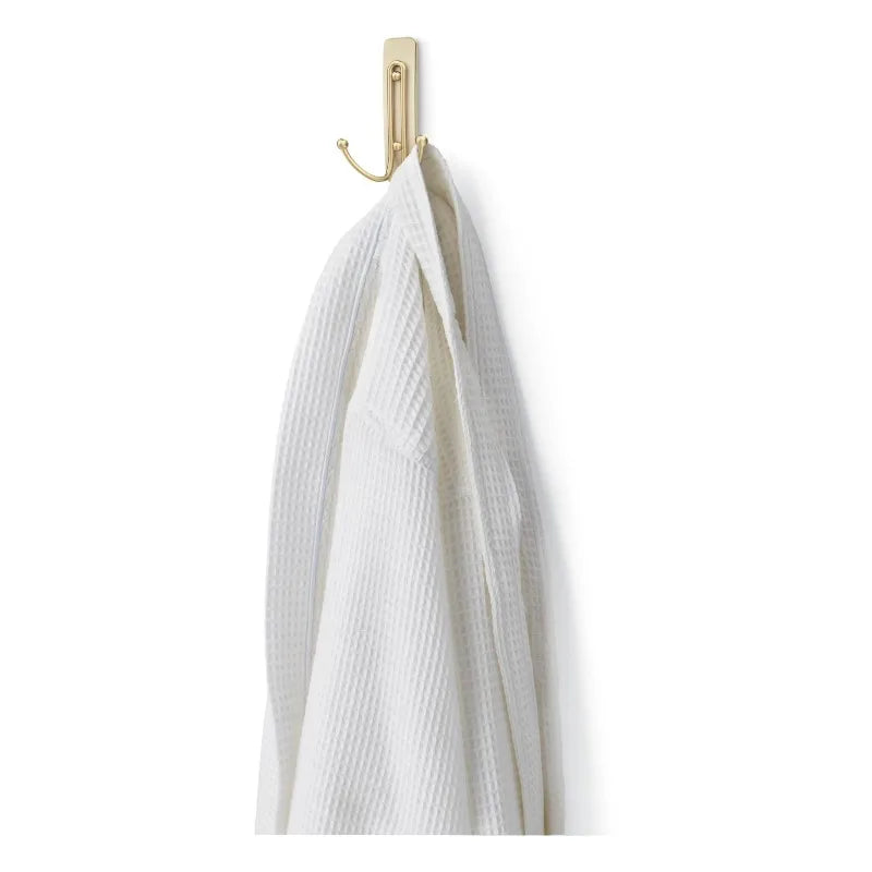 Bath satin-brass double hook mounted on wall holding a white towel