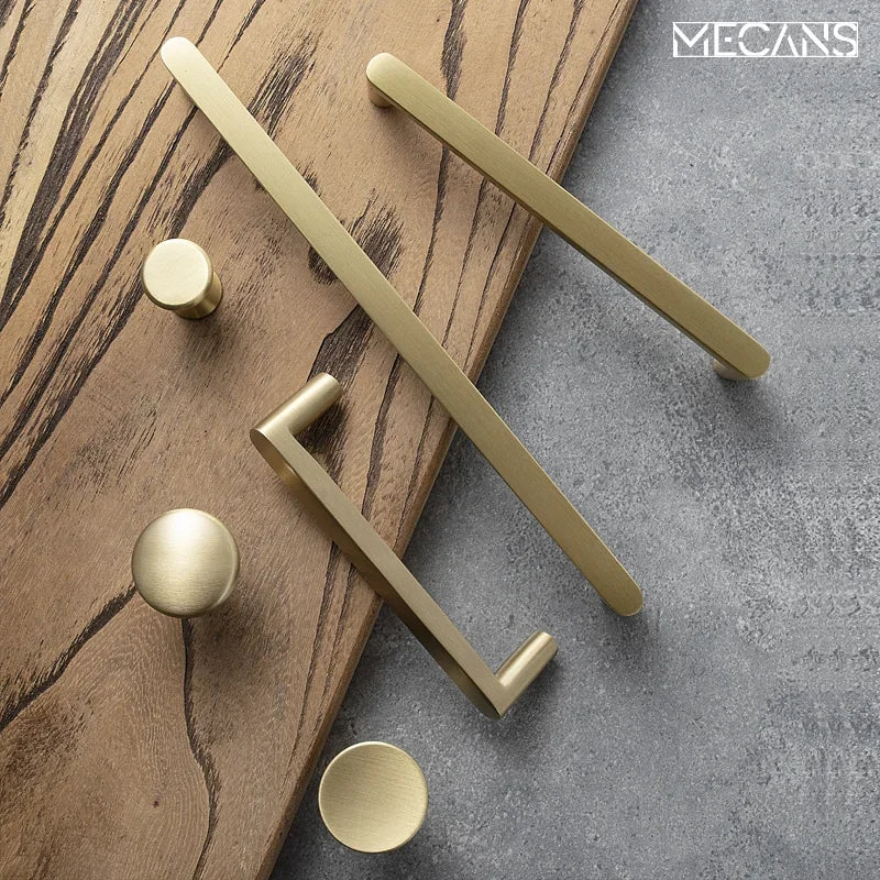 Solid brass cabinet pulls and round knobs set on wood and concrete backdrop