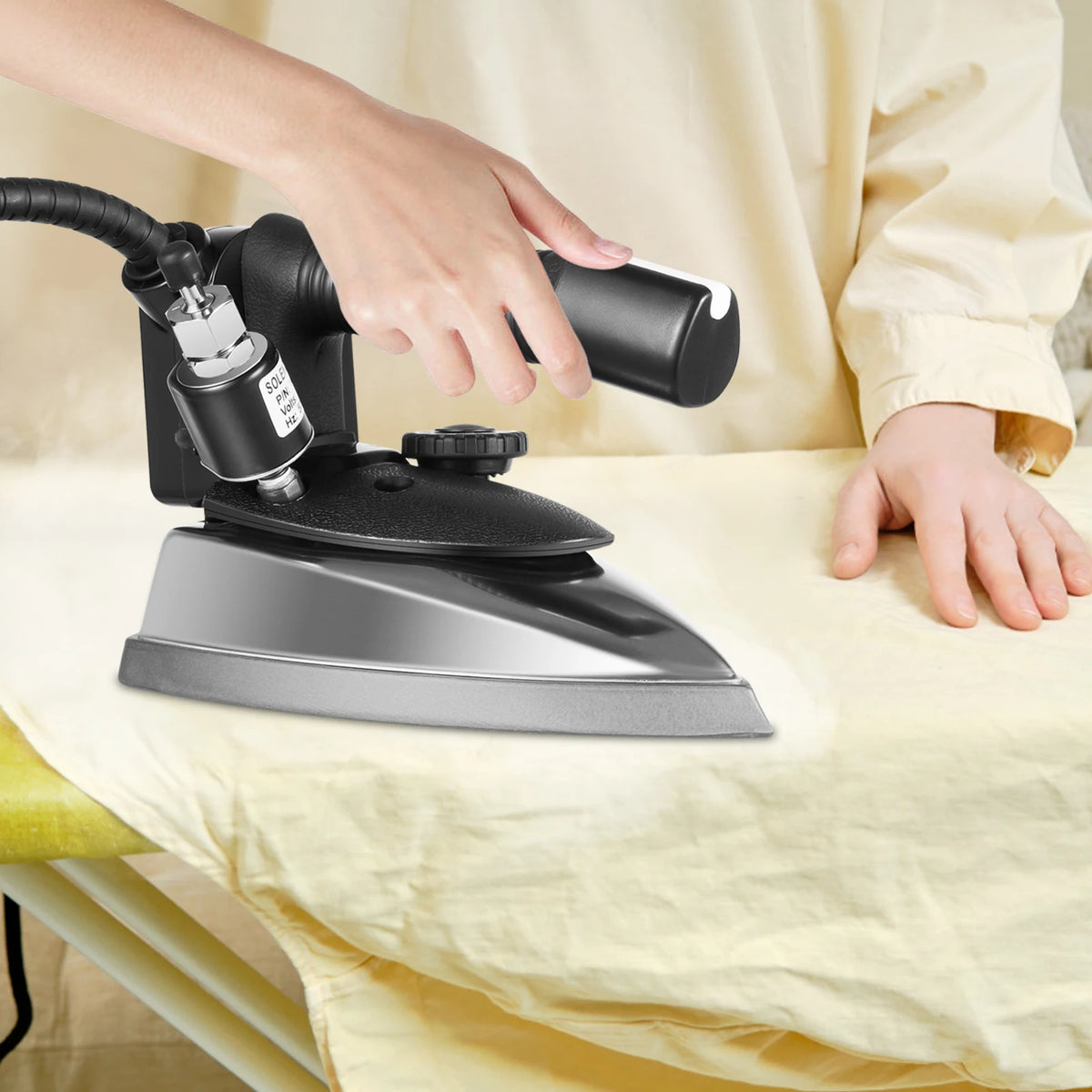 1200W electric steam iron by S And B Enterprise; black and silver iron used on beige fabric.
