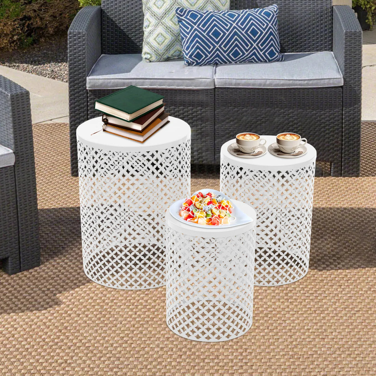 Three white metal lattice end tables for outdoor use, shown with books, coffee cups, and a dessert plate.