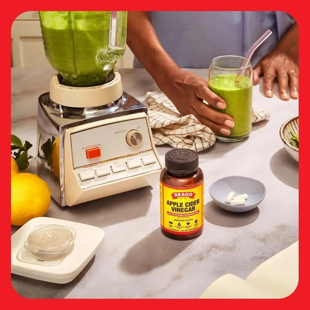 Bragg Apple Cider Vinegar capsules; two white capsules in a dish beside a blender with a green smoothie