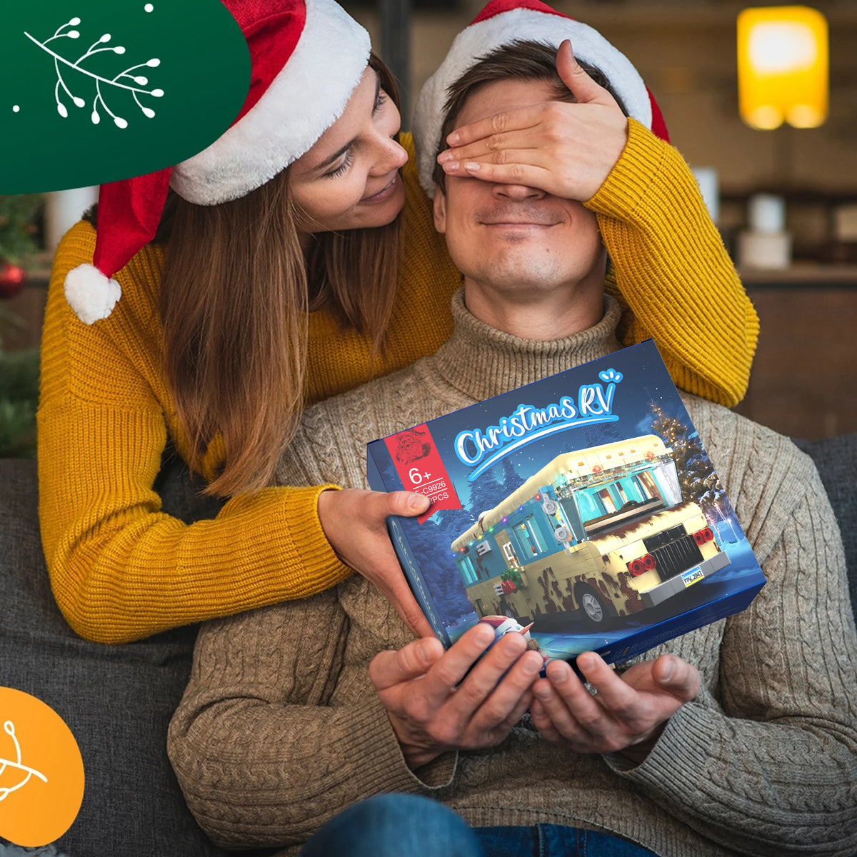 Christmas RV building blocks set held by a smiling couple in mustard yellow sweaters and Santa hats