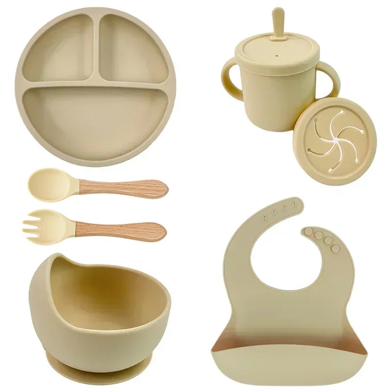 Beige 6-piece silicone child dish set including divided plate, cup with lid and straw, spoon, fork, suction bib.