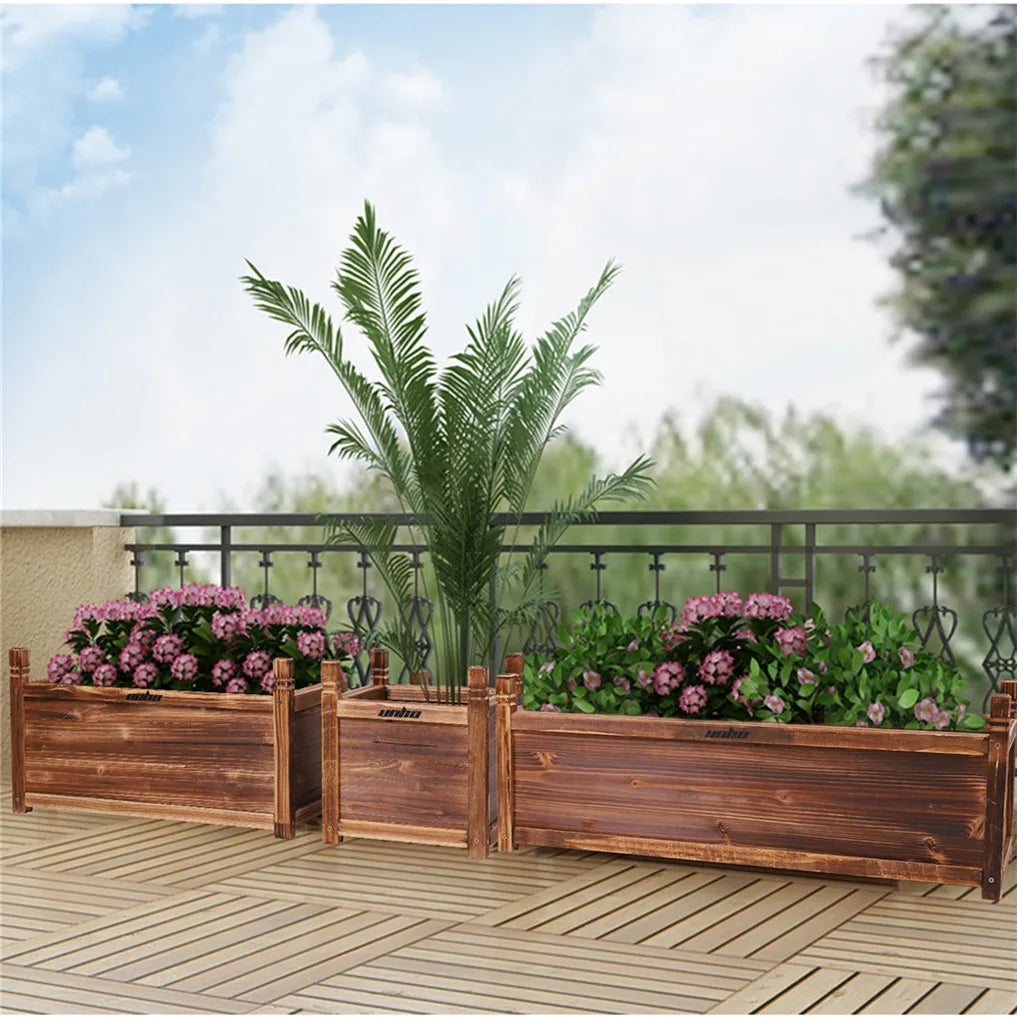Three wooden raised planter boxes for indoor/outdoor use on a balcony, filled with pink flowers and a tall palm.