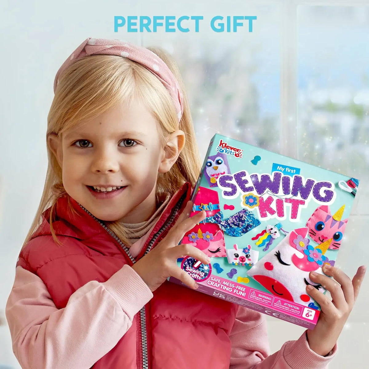 Kids sewing kit box with unicorn and mermaid artwork held by smiling girl; Klever Kits My First Sewing Kit