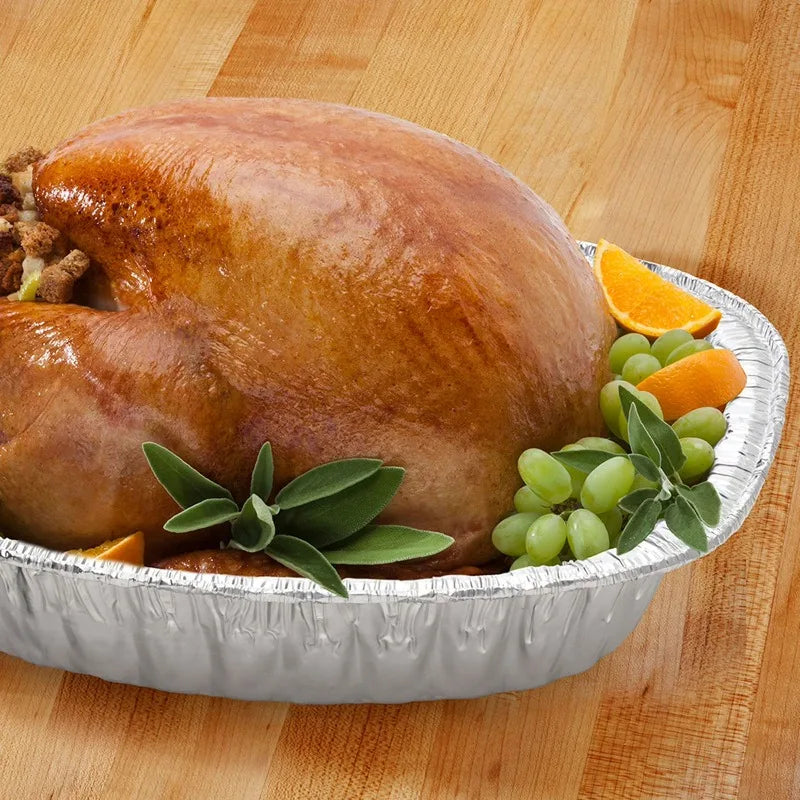 Aluminum extra-deep oval roaster pan holding a roasted turkey with orange slices and grapes.