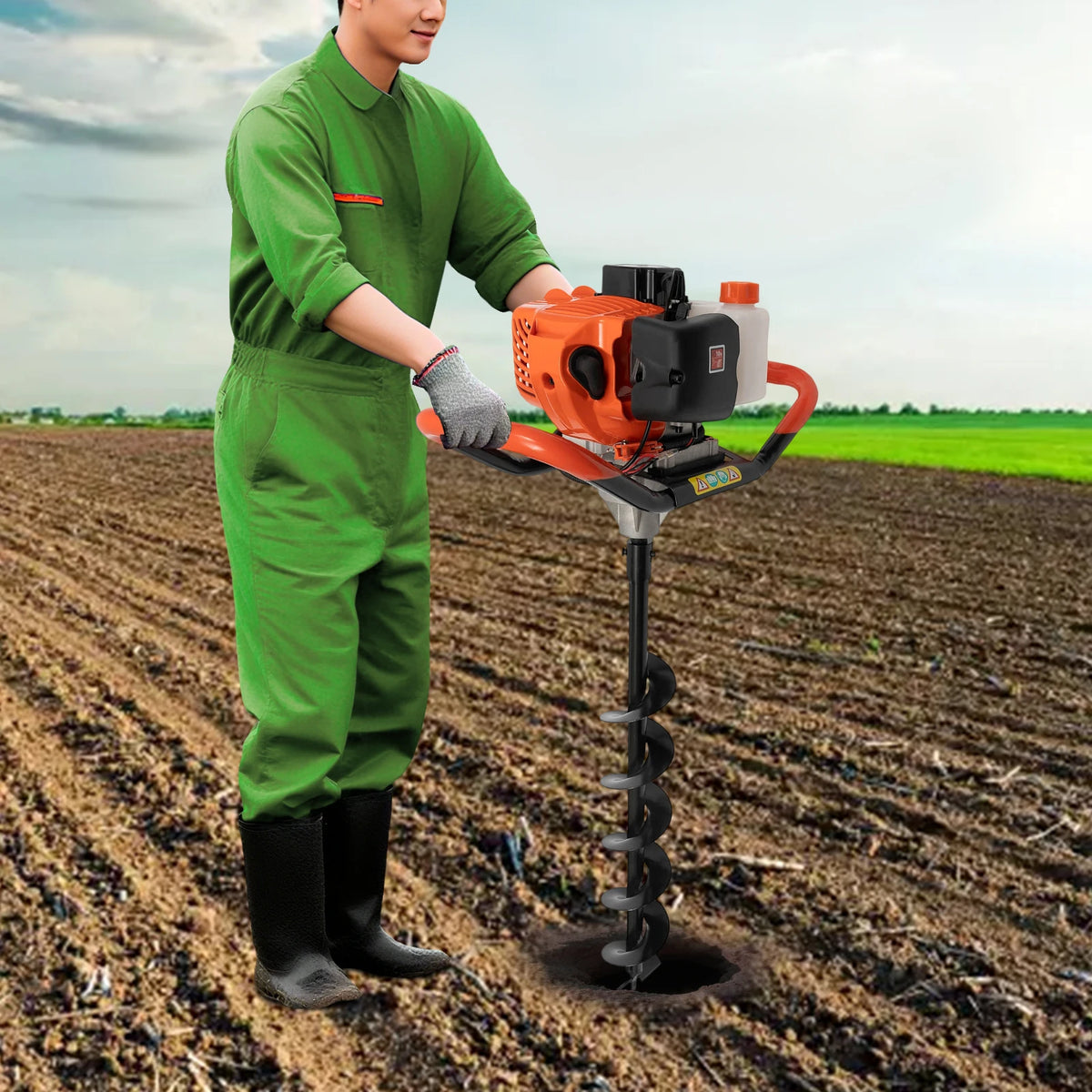 Post hole digger auger with orange petrol engine and 4/6/8 in bits, operator in green coveralls in a field