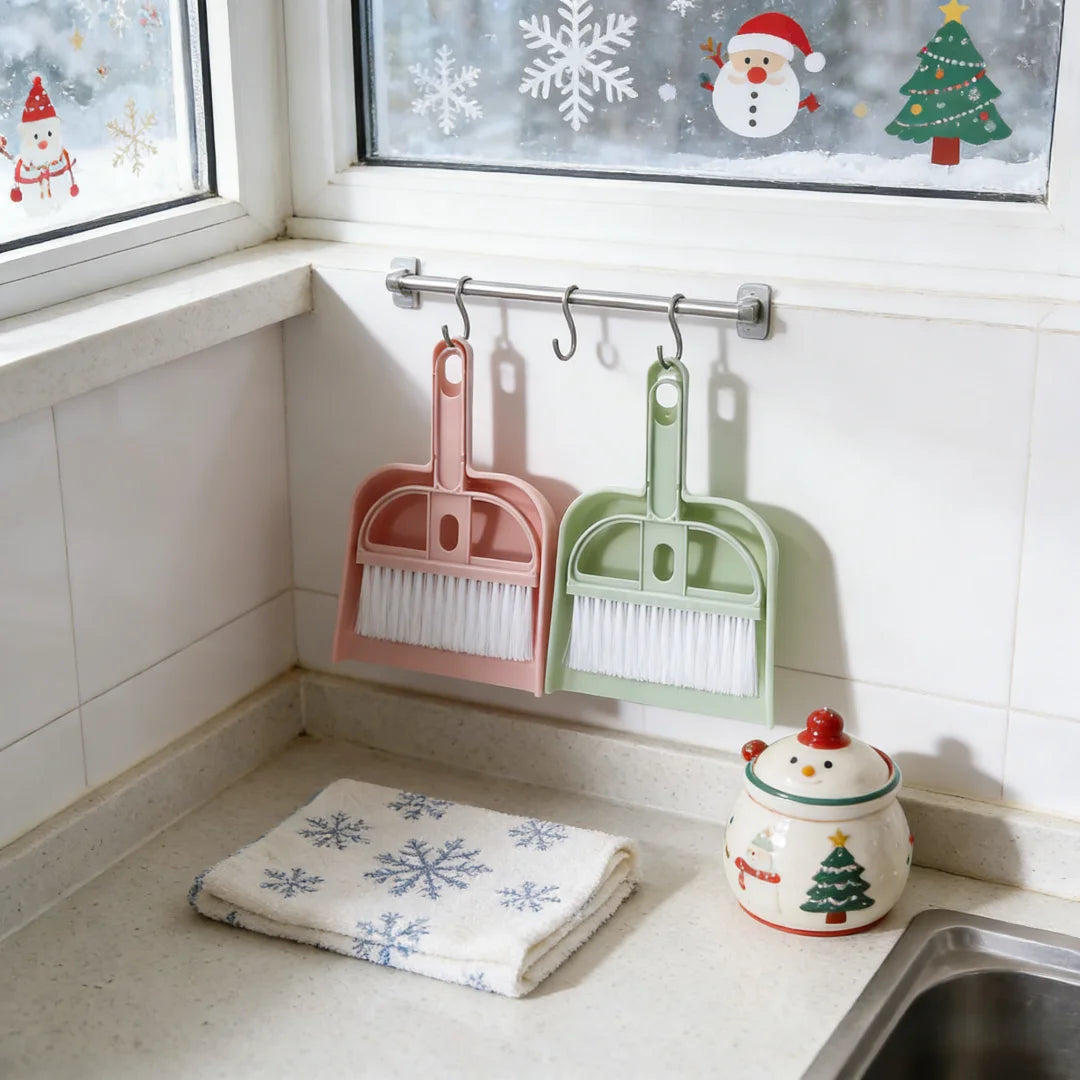 Mini desk broom and dustpan set in pink and green, hanging on a kitchen rail by S And B Enterprise.