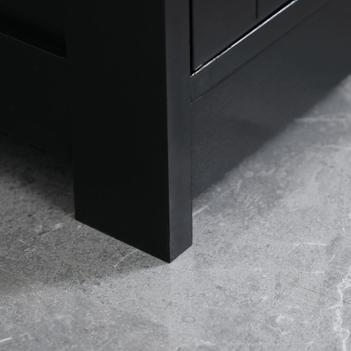 Under-sink bathroom cabinet leg in black on gray floor, close-up view
