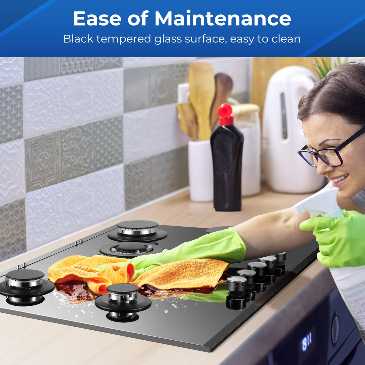 30-inch black glass gas cooktop with 5 burners on a kitchen counter being cleaned.